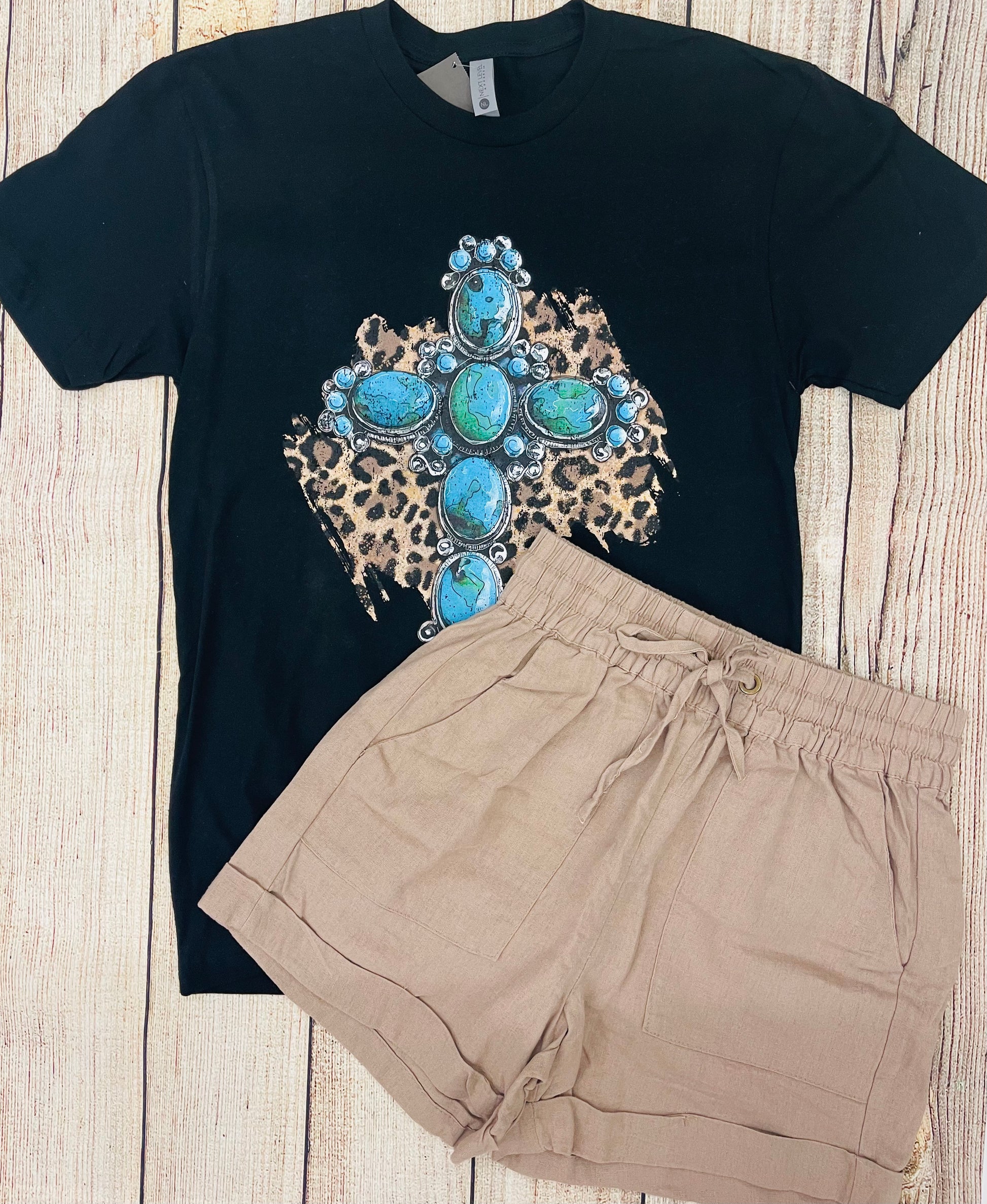 This is a black tee with a colorful graphic featuring a leopard background with a stone turquoise cross. It is a regular unisex fit with a crew neckline.
