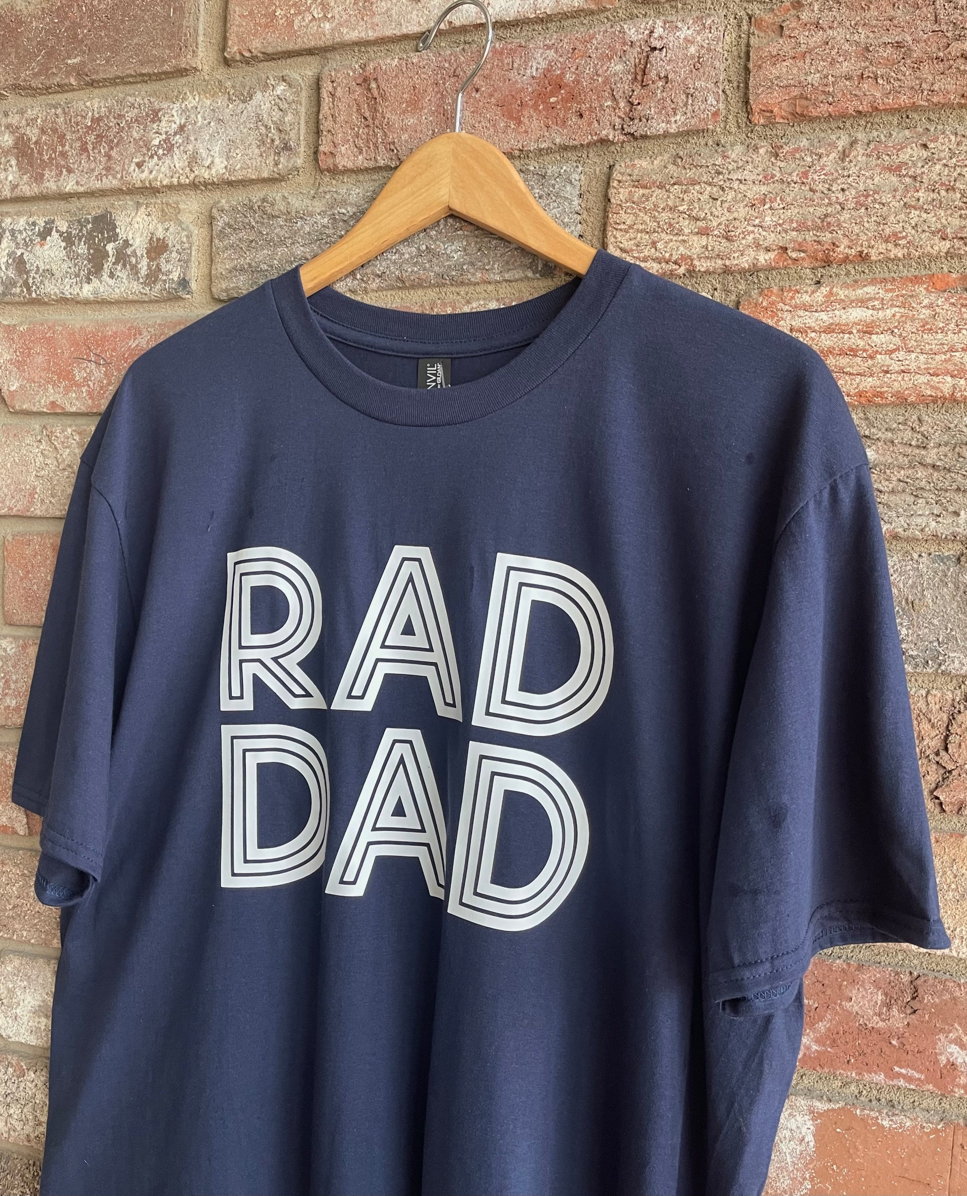 This is a navy blue unisex style tee with lettering, stating, "RAD DAD" on the front. It is a regular fit with a crew neckline. Looking for a fun tee for Father's Day? Look no further!